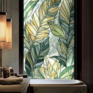 May include: A bathroom window featuring a stained glass design with large, stylized leaves in shades of green and yellow. The window is framed in dark wood, and a bathtub is visible below. The overall theme is nature and tranquility.