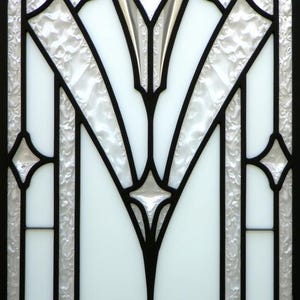 May include: Close-up of a stained glass window with a black geometric design. The design features a central floral motif and symmetrical patterns. The glass is a mix of clear, textured, and opaque white panels.