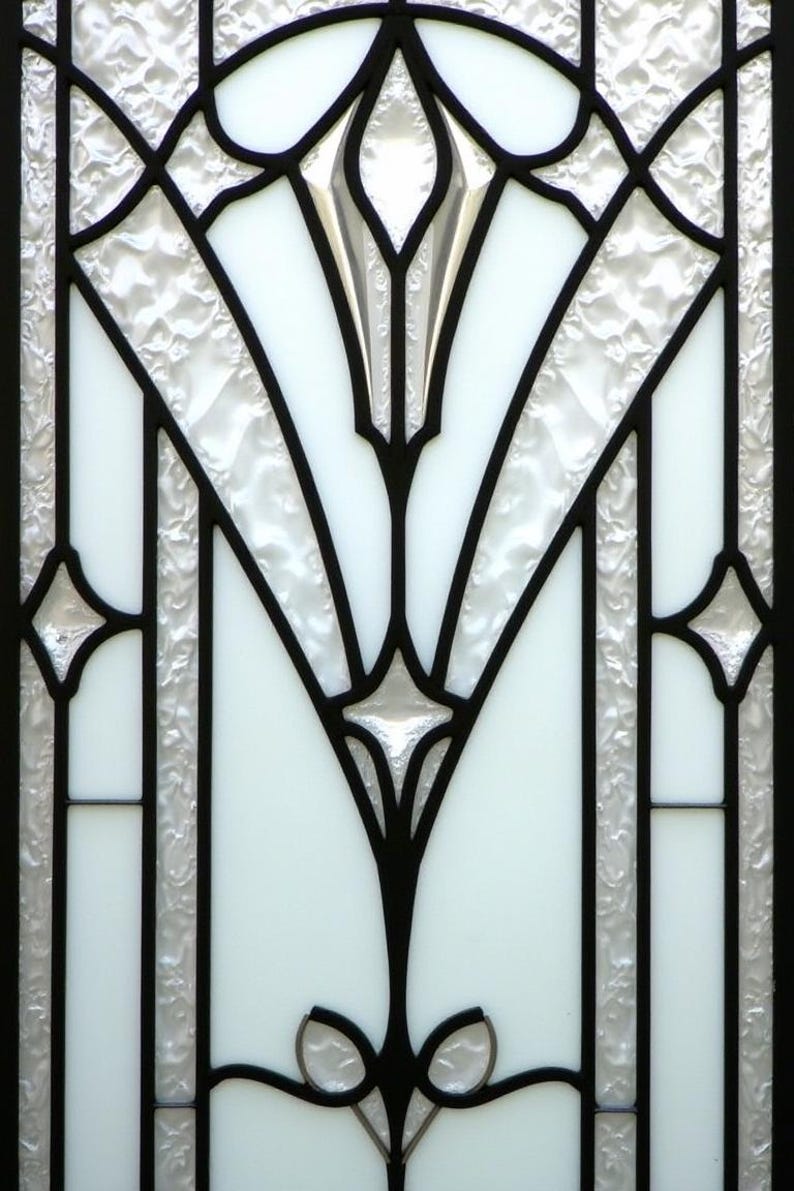 May include: Close-up of a stained glass window with a black geometric design. The design features a central floral motif and symmetrical patterns. The glass is a mix of clear, textured, and opaque white panels.
