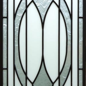 May include: A rectangular window with a decorative design. The window features a black metal frame with white and textured glass panels. The design includes geometric shapes and curved lines, creating a symmetrical pattern.