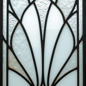 May include: A decorative window panel featuring a stylized floral design. The design incorporates white, textured glass sections framed by black metal lines. The overall pattern is symmetrical and reminiscent of Art Deco style.