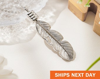 May include: A silver feather pendant necklace. The pendant is a detailed feather design with a textured surface and a small hole. The necklace is on a delicate silver chain. The image includes the text "SHIPS NEXT DAY".