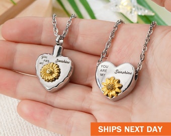 May include: Two silver heart-shaped cremation necklaces with sunflower charms. The necklaces are engraved with the text "You are my Sunshine".