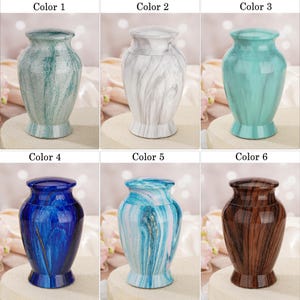 May include: A collection of six decorative urns, each featuring a distinct finish: a textured green, a white marble pattern, a solid teal, a deep blue with gold accents, a light blue and white swirl, and a dark brown wood grain pattern.