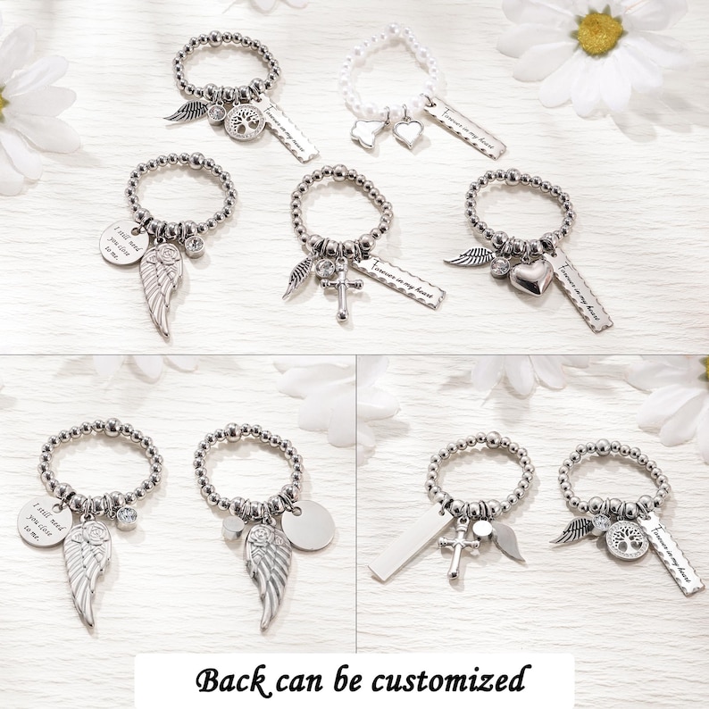 May include: A collection of beaded rings featuring silver-toned charms including angel wings, hearts, crosses, and tree of life motifs. Some rings include rectangular tags with the engraved text "Forever in my heart" or circular tags with "I still need you close to me."