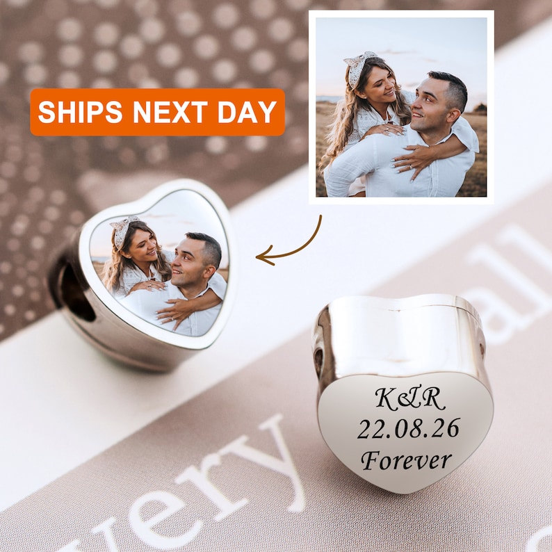 May include: Silver heart-shaped charm with a photo of a couple on one side and an inscription that reads "K&R 22.08.26 Forever" on the other side.