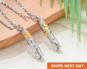 May include: Two silver necklaces with sunflower pendants. The pendants are cylindrical and have a gold sunflower design.