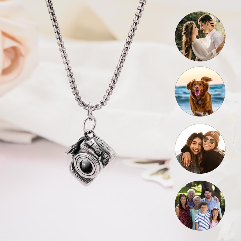 May include: A silver-toned metal camera pendant hangs from a matching box chain necklace. The camera charm features detailed engravings of lens and shutter components. To the right, four circular insets display various personal photographs.