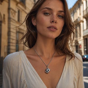 May include: A silver-toned necklace featuring a small, detailed camera pendant suspended from a delicate chain. The pendant is shaped like a classic camera with a prominent lens and rectangular body, resting against a light-colored, textured fabric.