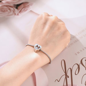 May include: A silver bracelet with a heart-shaped charm. The charm has a small opening in the center.
