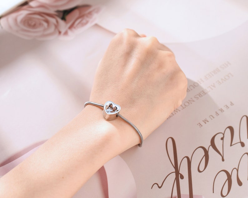 May include: A silver bracelet with a heart-shaped charm. The charm has a small opening in the center.