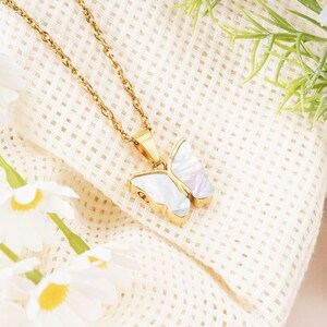 May include: A gold-toned metal chain necklace featuring a butterfly-shaped pendant. The pendant has a polished gold-colored metal frame and iridescent white mother-of-pearl inlay on the wings, suspended from a twisted rope-style metal chain.
