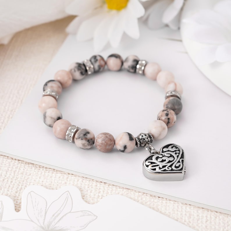 May include: A pink and white beaded bracelet with a silver heart charm. The heart charm has a filigree design.