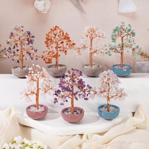 May include: A collection of gemstone trees in various colors, including purple, orange, white, and turquoise. Each tree has a copper wire trunk and branches, with the gemstones forming the leaves. The trees are potted in small ceramic bowls.
