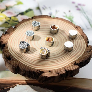 May include: A set of seven silver charm beads with various designs, including a paw print, a heart, and a round bead with a photo inside. The beads are arranged on a wooden surface.