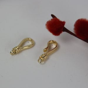 May include: Two gold-toned metal clasps, one with a loop and the other with a hook, on a white background.