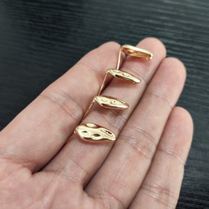 May include: Four gold-toned metal earring findings with a textured oval shape and a small loop at the top.