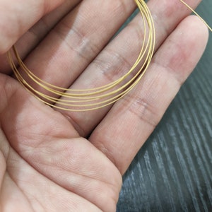 Può includere: Primo piano di una mano che tiene un fascio di filo color oro. Il filo è sottile e sembra essere di metallo.