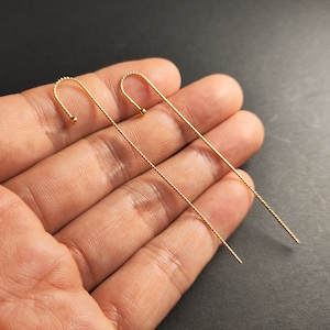 May include: A pair of gold-toned long earrings with a delicate chain design and a small ball at the end of each earring.