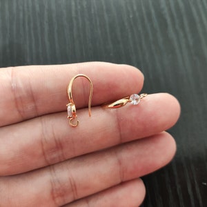 May include: A pair of gold-tone earring hooks with clear crystal accents. The hooks are designed with a small loop at the top for attaching earrings.