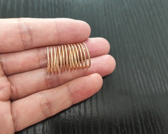 May include: A collection of gold-colored rings with a textured, dotted pattern. The rings are held in a hand, showcasing their delicate design. The rings are likely for jewelry or crafting.