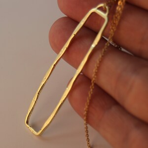 May include: A gold-toned necklace with a long, rectangular pendant. The pendant has a rough, textured surface.