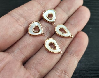 May include: Four gold-toned metal charms with white shell inlays. Each charm has a different shape, including a teardrop and a triangle. The charms have a hole at the top for attaching to jewelry.