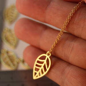 May include: A gold chain necklace with a delicate leaf pendant. The leaf is cut out and has a detailed design.