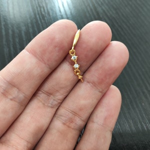 Könnte beinhalten: Goldener Ohrring mit drei klaren Strasssteinen in einem geschwungenen Design.