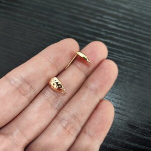 May include: Two gold-toned earring findings with a hammered texture. The findings have a loop on one end and a post on the other.