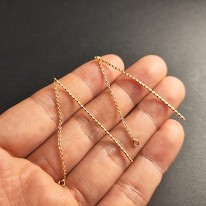 May include: Three gold chain extenders with jump rings at the ends. The chains are different lengths and have a twisted design.