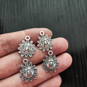 Puede incluir: Cuatro colgantes de sol plateados con un diseño de cara. Cada colgante tiene un bucle en la parte superior para sujetarlo a un collar o pulsera.