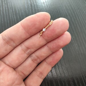 Könnte beinhalten: Ein goldener Creolenohrring mit einem kleinen, klaren Edelstein, der daran hängt. Der Ohrring wird in einer Hand gehalten.