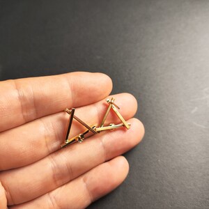 May include: A pair of gold triangle earrings with a geometric design. The earrings are small and delicate.