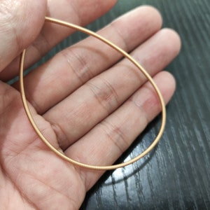 Op de afbeelding: Een gouden metalen gitaarsnaar, opgerold tot een cirkel, wordt in de hand van een persoon gehouden.