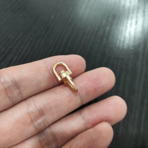 May include: Gold-toned metal swivel hook with a rounded loop. The hook is designed to attach to a bag or other item.