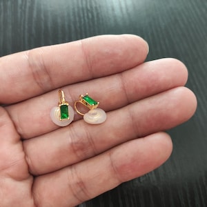 May include: A pair of gold earrings with green rectangular gemstones. The earrings are on a white background.