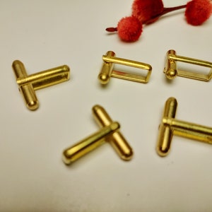 May include: Five gold-toned cufflinks, four are rectangular with rounded edges and one is a T-shape.