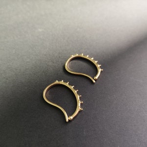 May include: A pair of gold hoop earrings with a curved shape and small clear stones around the edge.