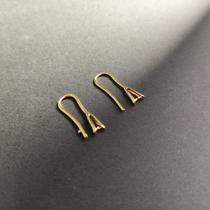 May include: Two gold-toned earring hooks, also known as ear wires, are shown on a black surface. The hooks are made of metal and have a simple, elegant design.