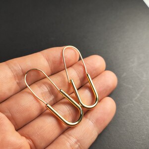 May include: A pair of gold-toned hoop earrings with a unique U-shaped design. The earrings are simple and elegant, making them a versatile accessory for any occasion.