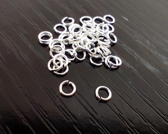 May include: A pile of silver jump rings, some are stacked on top of each other, and two are laying flat on a black surface.