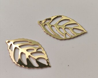 May include: Two gold leaf-shaped metal charms with a cutout design. The charms are on a white background.