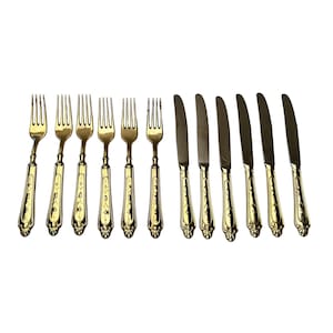 May include: A collection of antique gold-coloured forks and knives. The forks have four tines and decorative handles. The knives have a simple blade design with matching handles. The cutlery is arranged on a white background.