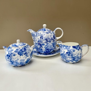 以下が含まれることがあります： 青と白の花柄が施された陶磁器のティーセット。セットには、お揃いのソーサーに乗った蓋付きのティーポット、両側に取っ手が付いた蓋付きのシュガーボウル、そしてミルクピッチャーが含まれており、すべて詳細なバラのモチーフで装飾されています。