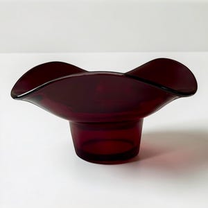 May include: A deep burgundy glass bowl with a wavy, flared rim. The bowl has a cylindrical base and a smooth, glossy finish. The design is simple and elegant, suitable for decorative use.