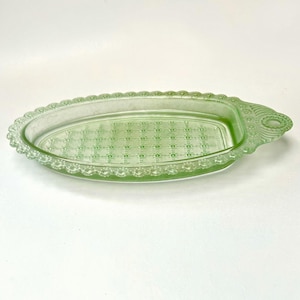 May include: A light green oval glass dish featuring a textured grid pattern on the base and a scalloped beaded edge. The dish includes a small handle on one end with a circular cutout and decorative embossed detailing around the rim.