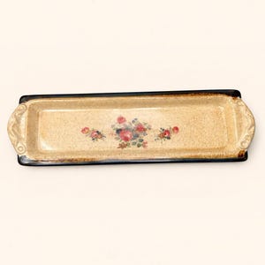 May include: A rectangular ceramic serving tray with a speckled beige finish and a dark brown rim. The centre features a floral motif with pink roses and green leaves. The tray has integrated handles on both ends with a decorative scroll design.