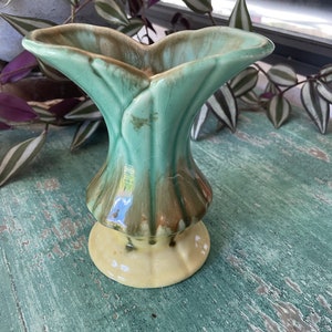 May include: A small, green and brown ceramic vase with a unique leaf-like design. The vase has a wide mouth and a narrow base.