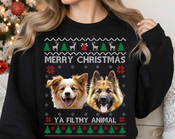 May include: Black sweatshirt with a festive Christmas design. The design includes the text "MERRY CHRISTMAS" and "YA FILTHY ANIMAL" along with images of dogs, reindeer, Christmas trees, and snowflakes. The sweatshirt is a cozy holiday themed apparel.